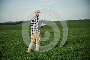 Walking, holding notepad. Handsome young man is on agricultural field