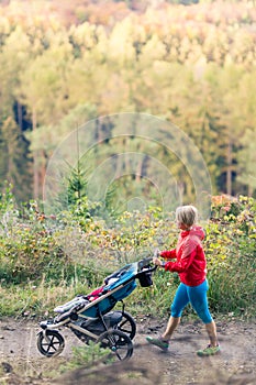 Walking mother with stroller enjoying motherhood at autumn sunset