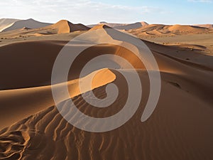 Walking on natural curved ridge line through wind blow pattern of rusty red sand dune with shade and shadow on desert landscape