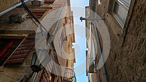 Walking on old town narrow street and looking up at the tiled roof and stone walls of ancient buildings and houses