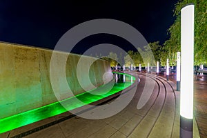 Walking path around fountain in resort with colored light illumination and trees on side at evening. Modern park design