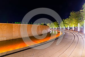 Walking path around fountain in resort with colored light illumination and trees on side at evening. Modern park design