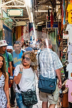 Walking people in ancient Old Town Market of Jerusalem full of shops with all kinds of touristic products like t-shirts, souvenirs