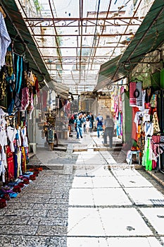 Walking people in ancient Old Town Market of Jerusalem full of shops with all kinds of touristic products like t-shirts, souvenirs