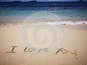 Walking on sandy beach and beautiful sunny day and I love you written on the the sandy beach