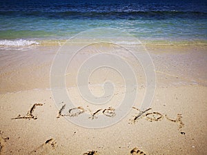 Walking on sandy beach and beautiful sunny day and I love you written on the the sandy beach