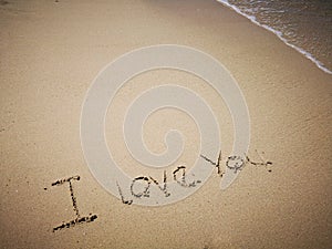 Walking on sandy beach and beautiful sunny day and I love you written on the the sandy beach