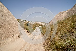 Walking unpaved rough sand trail route through desert mountain grass landscape of dried ancient red valley with clear sky