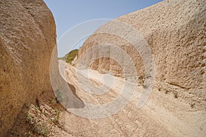 Walking unpaved rough sand trail route through desert mountain landscape of dried ancient red valley with clear sky background