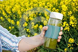 A walking woman is holding a glass bottle with prepared fruit and vegetables. smoothie, Delicious green drink. Blooming yellow