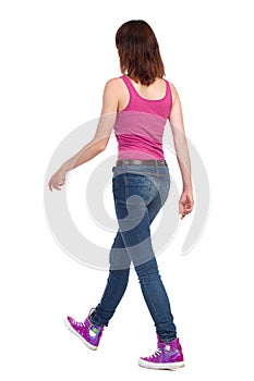 Walking Woman In Pink Tank Top. Jeans And Sneakers. Rear Side View.