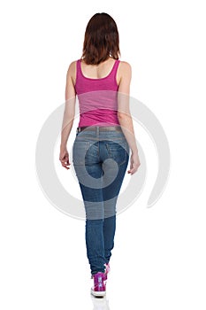 Walking Woman In Pink Tank Top. Jeans And Sneakers. Rear View