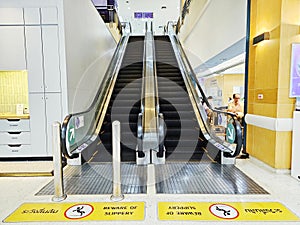 Walkway marked with yellow sidewalk with Beware of slippery floors signs at the way up and down the escalator