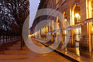 The wall of arches, columns and arcades bordering the Royal Palace Garden at rainy night. Paris. France.