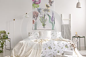 Wall art of flowers and birds painted on a fabric above a bed which is dressed in green plants pattern on white bedding in a fresh