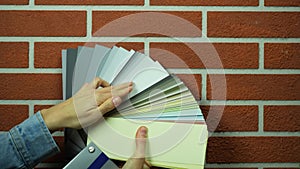 Wall with brick pattern in dark brown color. Color swatches palette in designer`s hand. Matching colors