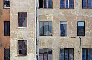 Wall of brown building with stailess steel water pipe and many different windows with various objects and people inside photo