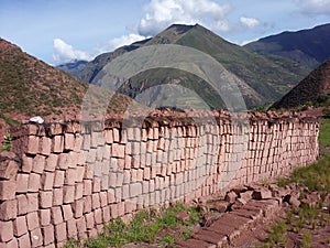 A wall of clay bricks next to Inca terraces of Moray. Peru