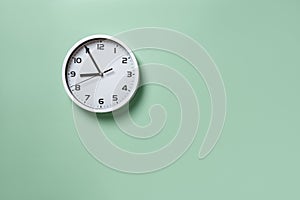 Wall clock hanging on the pale green wall with copy space. Round white clock with black hands. Five minutes to nine. Time