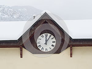 Wall clock with Roman numerals marking five minutes after noon