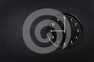 Wall clock showing nine o`clock on black chalkboard background. Office clock showing 9am or 9pm on black texture photo