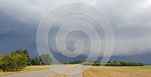 wall cloud of a thunderstorm above dry yellow fields and green trees in Laag Zuthem in Overijssel, the Netherlands.