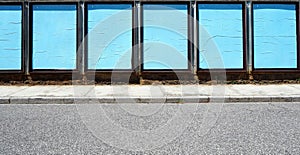 Wall covered with empty pale blue street billboards. Concrete sidewalk and asphalt road in front.