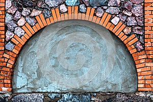 A wall of granite stones with a brick arch covered with paint