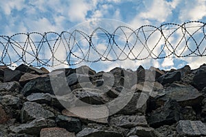 A wall of grey stone topped with barbed wire.