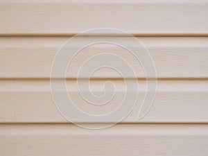 A wall of a house sheathed with plastic siding close-up. Light beige brown background or wallpaper. The material is faded and not