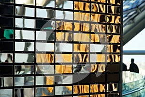 Wall made of polished metal mirrored rectangles imitating brickwork. Interior element and silhouette of people in the background.