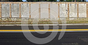 Wall made of rough cement and bricks. Grassy sidewalk and street with yellow and white traffic dividing lines