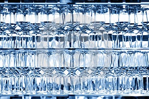 Wall of many empty transparent wine glasses on glass shelf at bar cafe restaurant against backlit window. Abstract alcoholic