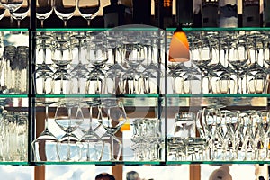 Wall of many empty transparent wine glasses on glass shelf at bar cafe or restaurant against backlit window. Abstract alcoholic