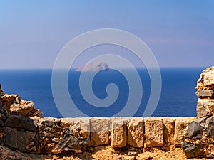 Wall of the medieval fortress that overlooks the sea and small lone island in the background