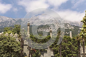 A wall with Moorish turrets, overgrown with lush greenery and a view of the peaks of AI-Petri in the clouds.