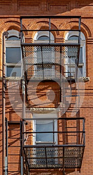 The wall of an old brick building with windows, balconies, and old iron staircase