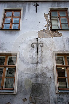 Wall of an old building with cracked stucco, forged decorative patterns and wooden windows.