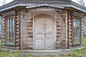 The wall of an old wooden house with large windows with carved platbands and a locked door