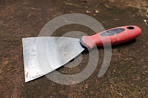 A wall paint scraper with a red and black handle