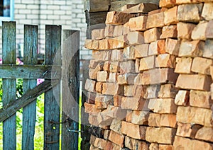 A wall of red and orange bricks stacked in rows outside in the courtyard near an old wooden door. The old brick. building material