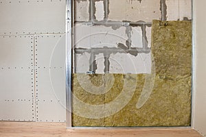 Wall of a room under renovation with mineral rock wool insulation and metal frame prepared for drywall plates