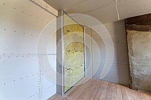 Wall of a room under renovation with mineral rock wool insulation and metal frame prepared for drywall plates