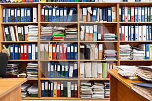 Wall from shelves with colourful file binders, an office room with papers and documents