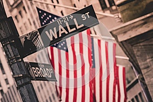 Wall street sign in New York with American flags and New York Stock Exchange in background