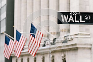 Wall Street sign post with American national flags in background. New York city financial economy district, stock market trade