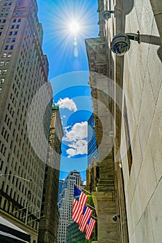 Wall Street, the sun in the sky illuminates the 3 American flags attached to the facade of building, Financial district