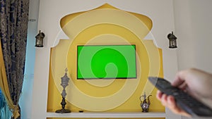 Wall with TV and green screen in the style of the Middle East and North Africa. Hand with remote control. FIFA Arab Cup