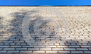 A wall of white bricks going up to the blue sky in the rays of the sun with shadow. Background Image