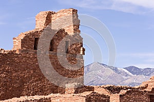 Wall and windows of Abo Ruins with Manzano Mountains in the distance. Full sunshine, blue sky